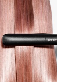 Zwarte stijltang ligt op gladde, roze haarstrengen en benadrukt het strakke design en de glanzende, rechte textuur.