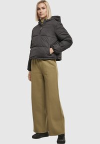 Sort dunjakke med hætte, lynlås og elastiske manchetter, kombineret med olivengrønne bukser med vide ben og sort fodtøj.