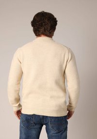 Crèmekleurige gebreide trui met een hoge kraag, geribbelde afwerking en lange mouwen, gecombineerd met blauwe denim jeans.