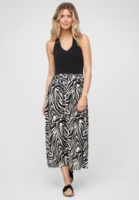 Haut à bretelles noir associé à une longue jupe fluide ornée d'un motif zèbre en noir et crème. Des sandales complètent le look.