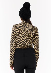 Maglietta a maniche lunghe beige con strisce zebrate nere, con colletto alto e design aderente, abbinata a pantaloni neri e un berretto di lana nero.