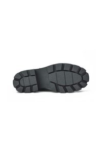 Suela de goma negra con surcos profundos, que presenta una superficie texturizada y un talón reforzado para ofrecer tracción y durabilidad.