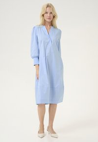 Gaiši zils, līdz ceļgaliem garš kleits ar V veida dekoltē, pūkainām piedurknēm un taisnu siluetu. Izgatavots no gludas šķiedras ar minimālu apdari.