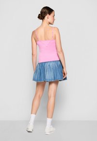 Rosa camisetto med justerbare stropper og V-formet rygg, kombinert med en plisserte denimskjørt. Hvite sneakers og sokker fullfører antrekket.