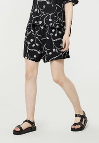 Svarta shorts med vitt blommönster, lös passform, ihop med svarta sandaler med remmar som har nitar och tjocka sulor.