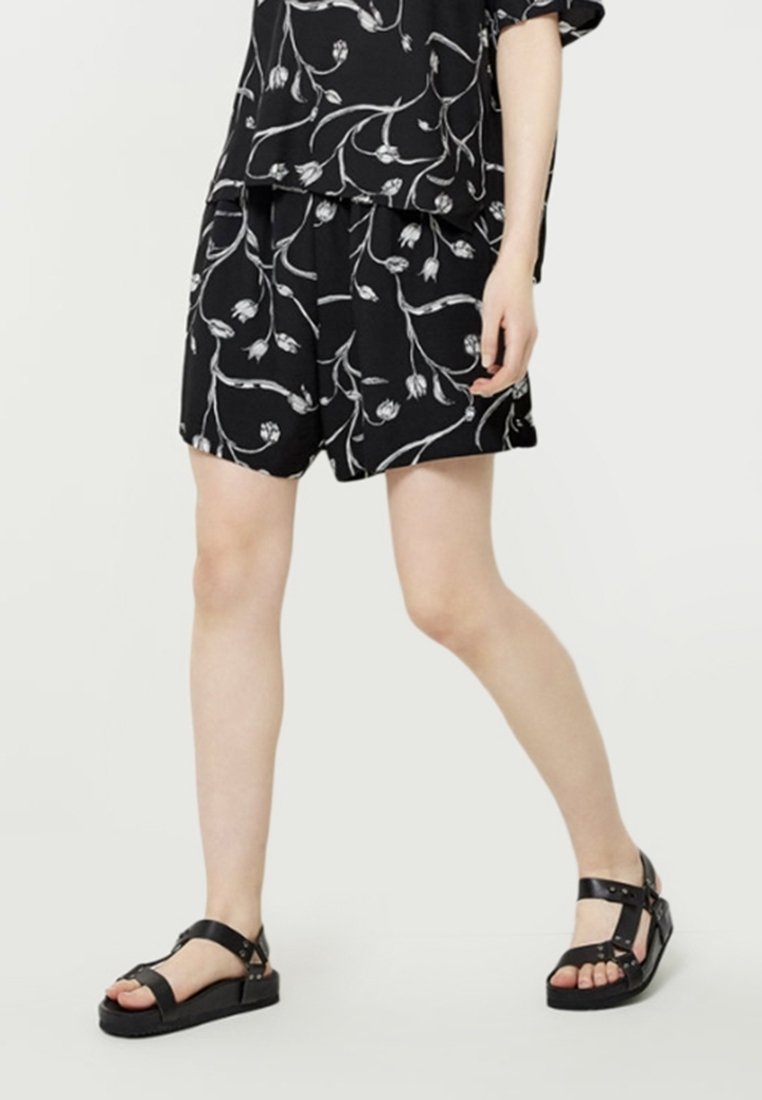 Svarta shorts med vitt blommönster, lös passform, ihop med svarta sandaler med remmar som har nitar och tjocka sulor.