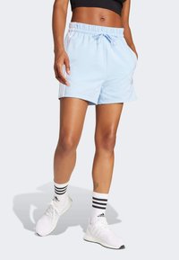 Shorts de sport bleu clair avec une taille élastique, un cordon de serrage, des poches latérales et trois bandes blanches de chaque côté.