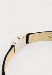 Caixa de relógio quadrada prateada com um mostrador texturizado, apresentando uma pulseira de camurça preta e um lado inferior em couro castanho. A pulseira possui uma fivela metálica.