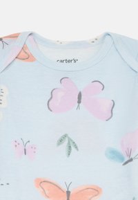 Svijetloplavi pamučni kombinezon s printom leptira i lišća u ružičastoj, narančastoj i zelenoj boji. Oznaka kaže "carter's." Mekani, kratki rukavi.