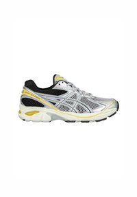 Zapatilla de running plateada con parte superior de malla, acentos en negro y detalles en amarillo. Suela elevada con agarre texturizado en el exterior.