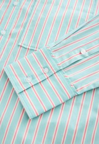 Camisa de botón azul claro con rayas verticales en rosa y blanco. Presenta un cuello con puntas y un detalle de puño con un solo botón. Material de algodón.