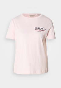 T-shirt en coton rose avec un col rond. Présente le logo "GANT 1949" en bleu marine et rouge sur la poitrine, des manches courtes et un ourlet droit.