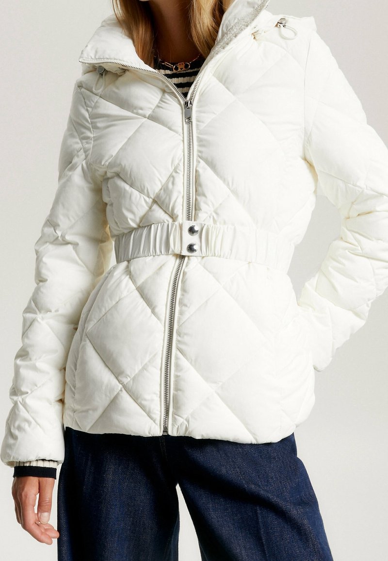 Chaqueta acolchada blanca con cierre de cremallera, cintura ceñida destacada con cinturón y cuello alto. Presenta costuras diagonales y dos bolsillos laterales.