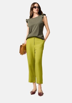 Top verde oliva con maniche a volant e decorazioni, abbinato a pantaloni su misura verde brillante e ballerine borgogna a punta.