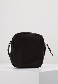 Černá křížová taška vyrobená z odolného nylonu s texturovaným povrchem, která má zipové uzavření a nastavitelný popruh.