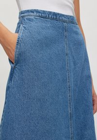 Denim rok met een middelmatige wassing, A-lijnvorm, zichtbare stiksels langs de naden en zijzakken. Textuurstof met een klassiek ontwerp.