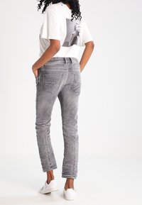 Szare dżinsy o dopasowanym kroju, z pięcioma kieszeniami i lekko zniszczonym wykończeniem. W zestawie z białą koszulką z graficznym nadrukiem na plecach.