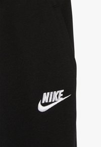 Närbild av svart tyg med en vit broderad Nike-logotyp och swoosh i nedre högra hörnet.