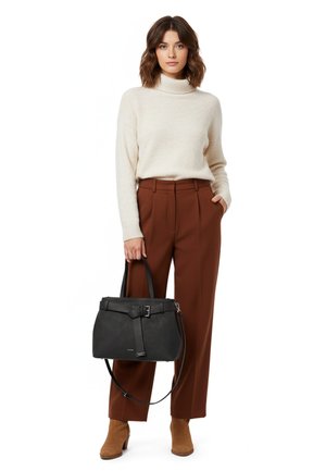 Moteris vilki kreminės spalvos golfą ir rūdžių spalvos kelnes, laiko juodą rankinę, dėvi rudus aulinukus, stovėdama ant balto fono.