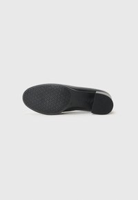 Black shoe with a smooth leather upper and a textured rubber sole. Rounded toe and low heel, featuring a subtle brand logo on the sole.