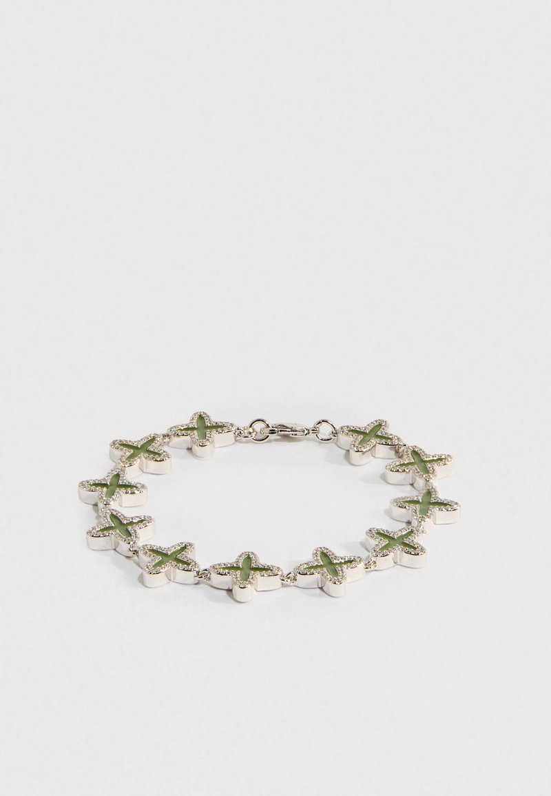 Pulseira de prata com pendentes verdes em forma de cruz ligados entre si, exibida sobre um fundo branco simples.