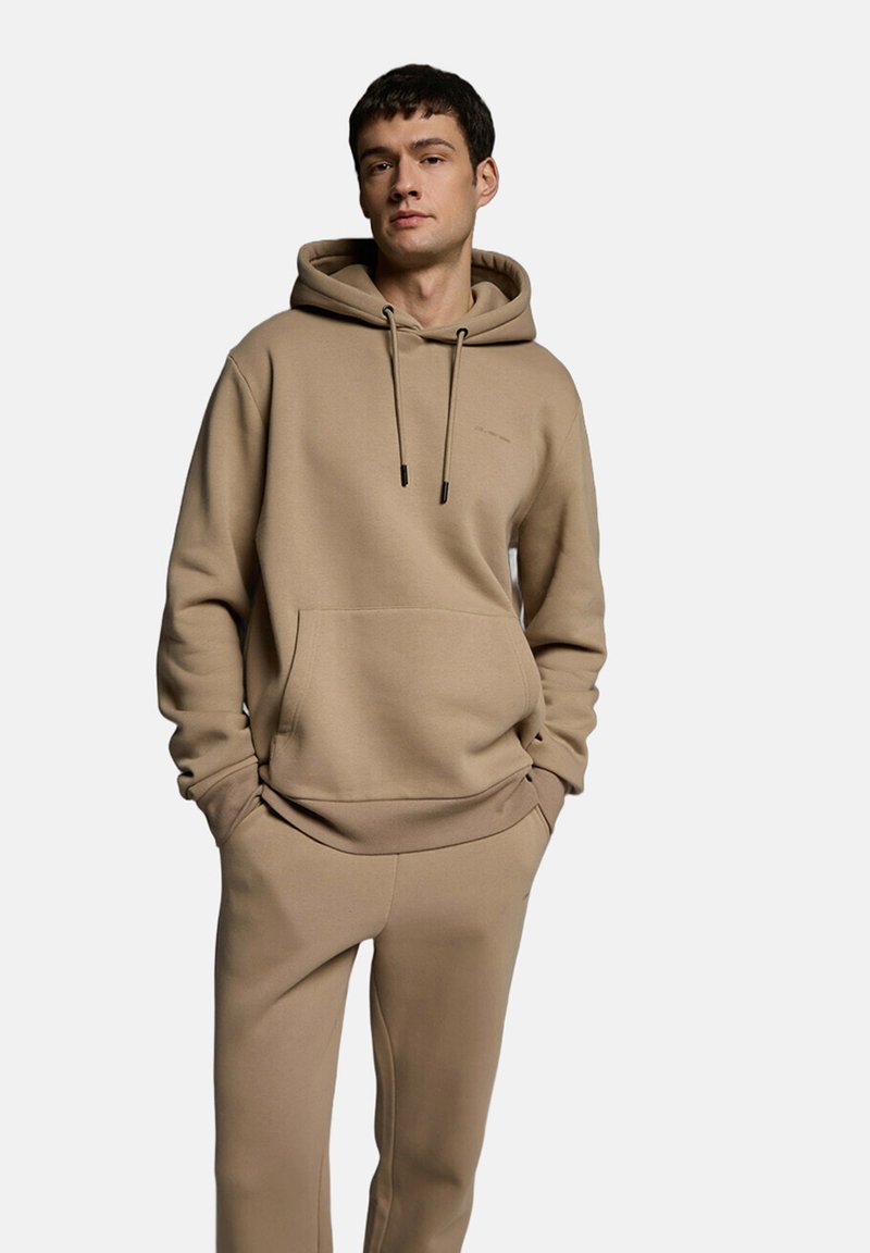 Beżowa bluza z kapturem wykonana z miękkiego materiału, z kieszenią kangurką, regulowanymi sznurkami i ściągaczami przy mankietach, zestawiona z pasującymi beżowymi dresami.