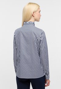 Mørkeblå og hvidstribet skjorte med knaplukning, høj krave, lange ærmer og en buet kant. Stoffet ser glat og struktureret ud.