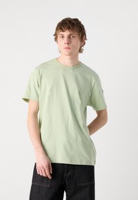 Light green cotton t-shirt with a round neckline and short sleeves, paired with dark denim pants featuring pockets and a relaxed fit.