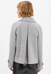 Grijze wollen jas met een notch-kraag, achterplooidetail en buttoned manchetten, ontworpen met een getailleerde pasvorm en een gladde textuur.