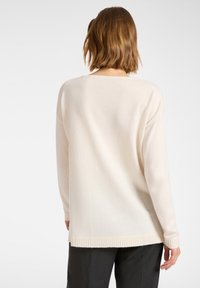 Kermanvärinen neulepaita, jossa on rento leikkaus, ribbaushelma ja pitkät hihat. Pehmeä rakenne, minimalistinen muotoilu ilman näkyviä kuvioita tai koristeita.