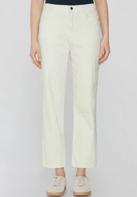 Pantalones de denim blancos con un diseño de pierna recta, que cuentan con cierre de botón, bolsillos frontales y una textura sutil. Combinados con zapatillas de color beis claro.