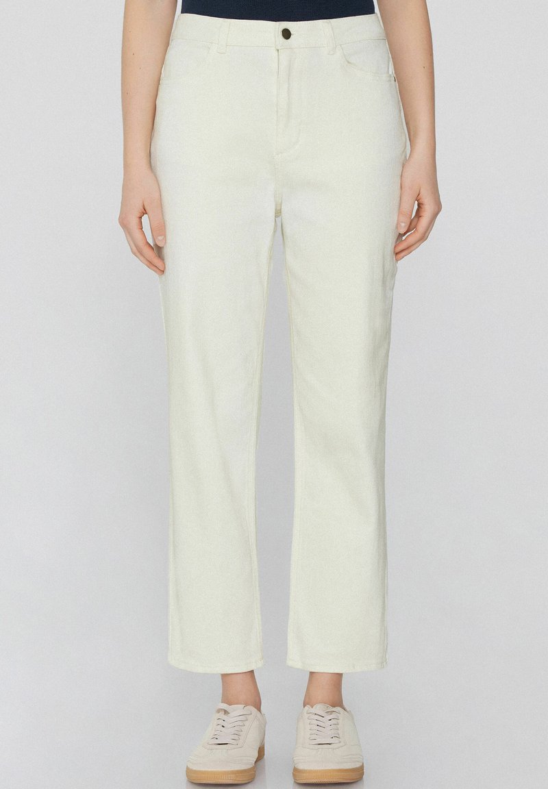 Pantalones de denim blancos con un diseño de pierna recta, que cuentan con cierre de botón, bolsillos frontales y una textura sutil. Combinados con zapatillas de color beis claro.