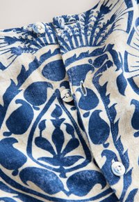 Sininen ja kerma valkoinen kuviollinen kangas, jossa kukkakuvioita. Kaulan kohdalla kolme nappia ja pehmeä, teksturoitu viimeistely.