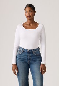 Λευκό κορμάκι μακρυμάνικο με τετράγωνη λαιμόκοψη, συνδυασμένο με ψηλόμεσο τζιν μπλε με κλασικό σχεδιασμό πέντε τσεπών.