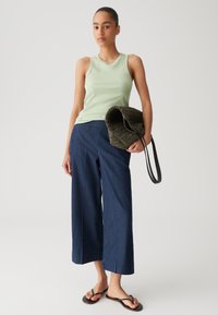Lichtgroen geribbelde tanktop, marineblauwe wijde broeken, zwarte flip-flops en een gestructureerde olijfgroene tas met een zwarte strap.