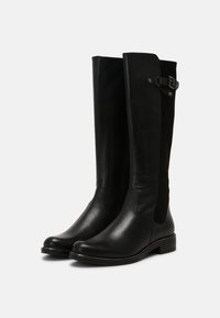 Bottes hautes en cuir noir lisse, avec des panneaux élastiques latéraux et une boucle décorative en haut. Bout arrondi et talon bas.