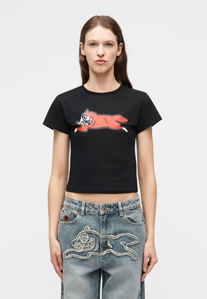 Γυναίκα που φοράει μαύρο κοντό μπλουζάκι με κόκκινο σκίτσο σκύλου που τρέχει και μπλε τζιν παντελόνι με διακοσμητική κεντημένη στάμπα σκύλου στο ίδιο μοτίβο.