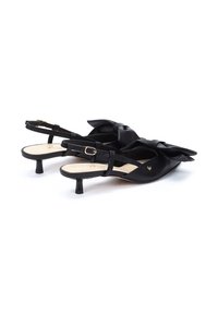 Zapatos slingback de cuero negro con un amplio detalle de lazo, tacón bajo y correa en el tobillo. Textura suave con plantilla beige. Detalles en dorado.