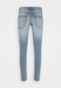 Jean skinny bleu clair délavé vu de dos avec deux poches arrière et des passants de ceinture sur un fond blanc uni.