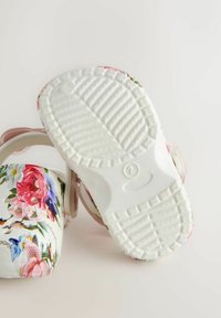 Lillelaste lillekirjaga sandaalid valgete talladega; omaduseks on helesinine rihm ja tekstuuriga põhi paremaks haarde saavutamiseks.