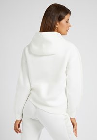 Vit hoodie med en avslappnad passform, som har huva, ribbade ärmslut och ett smidigt tyg. Kombinerad med matchande vita byxor, med minimala detaljer.