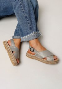 Zilveren kruisband sandalen met een gestructureerde bovenkant, gespsluiting en een natuurlijke jute platformzool, gedragen met versleten denim jeans.