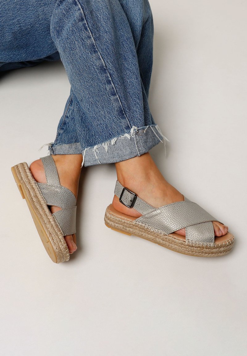 Zilveren kruisband sandalen met een gestructureerde bovenkant, gespsluiting en een natuurlijke jute platformzool, gedragen met versleten denim jeans.
