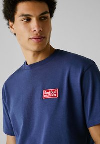 Marineblauwe katoenen T-shirt met een rode geborduurde 'Red Bull RACING' logo op de linkerborst, ronde halslijn en korte mouwen.