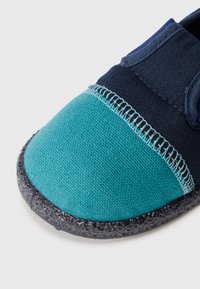 Blå och turkos tygskor med rund tå, texturerad svart gummisula, kontrasterande sömmar längs sömmen och en elastisk ovandel.