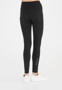 Mustat legginsit korkealla vyötäröllä, sileällä pinnalla ja logoyksityiskohdalla alaleuassa, yhdistettynä valkoisiin lenkkareihin.