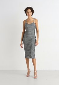 Robe midi grise froncée avec des bretelles fines réglables, silhouette sans couture et finition texturée, assortie à des talons transparents à lanières.