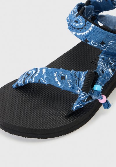 Σανδάλι με μαύρη υφή στη σόλα και μπλε υφασμάτινα λουράκια με σχέδια, στερεωμένα με ροζ και μπλε χάντρες.