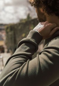 Felpa verde oliva con maniche lunghe, caratterizzata da polsini a coste e un sottile design ricamato sulla manica sinistra. Texture liscia.