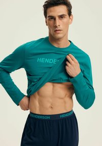 Koszulka z długim rękawem w kolorze teal z napisem "HENDERSON" drukowanym pogrubioną czcionką, w zestawie z granatowymi szortami z elastycznym pasem i dopasowanym logo.